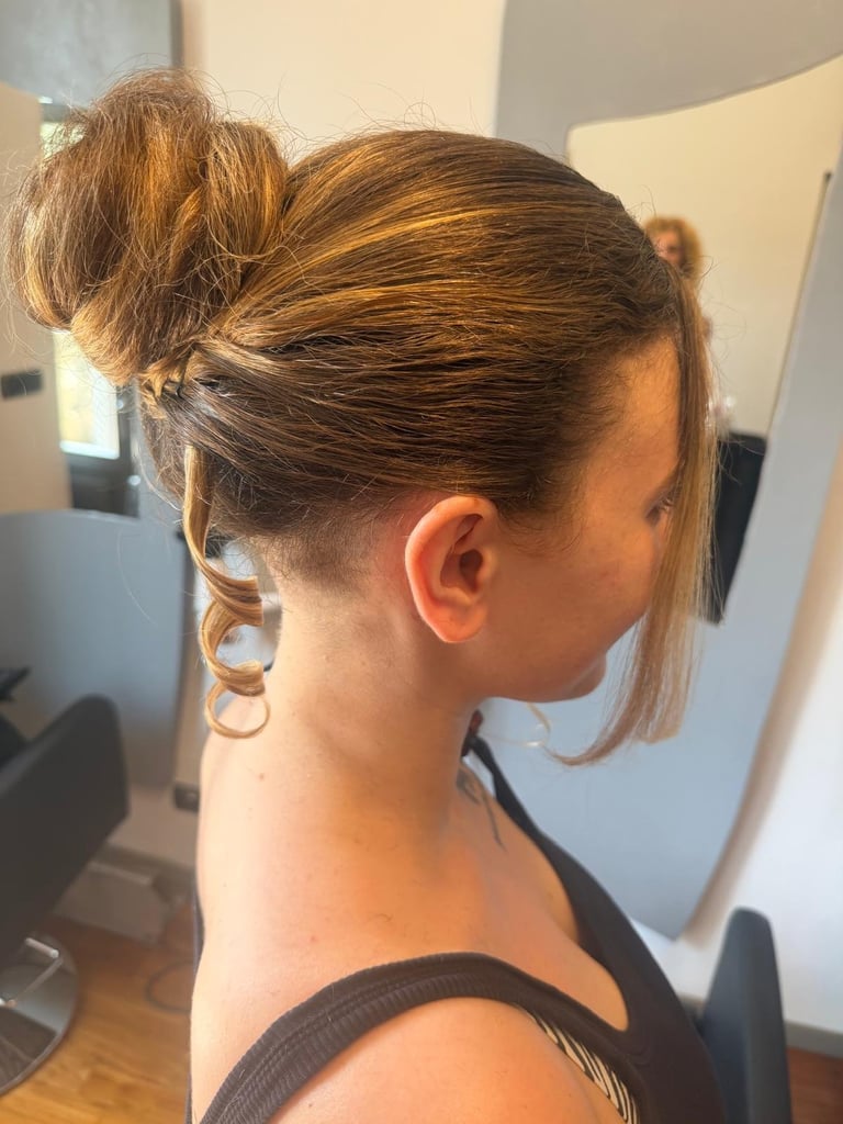 Person with brown hair styled in a top bun with shaved undercut sides, shown from behind in profile view
