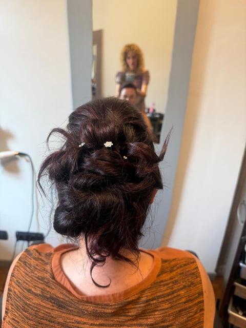 Back view of a woman with dark hair styled in an updo with decorative clips, wearing an orange striped top, photographed in a bathroom with mirror reflection