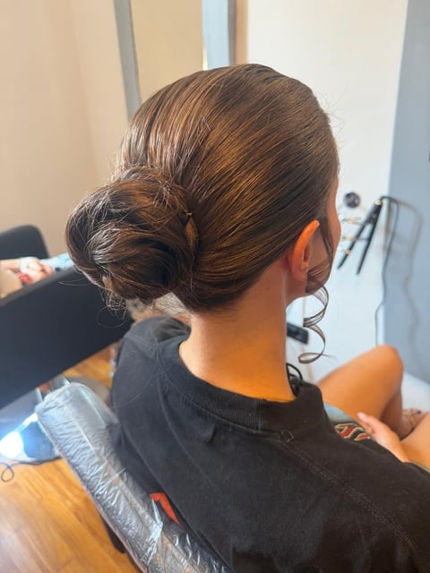Woman with medium brown hair styled in a low bun, viewed from behind, wearing a black shirt